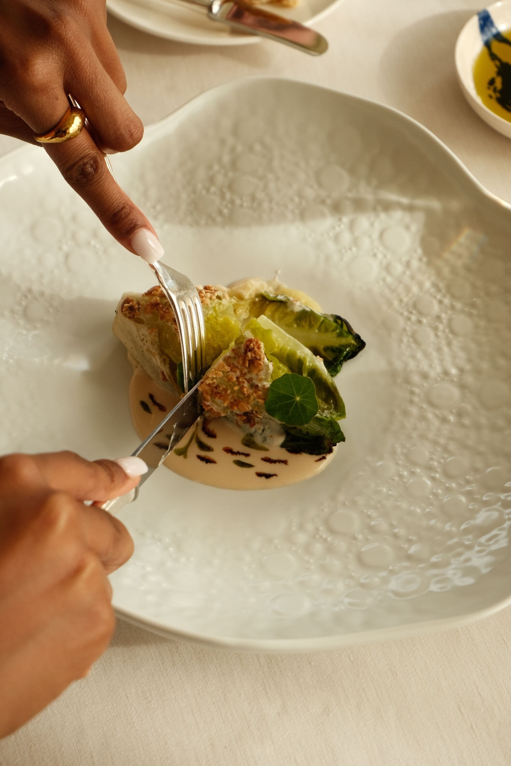 A person cutting a dish on a white plate with a textured pattern.