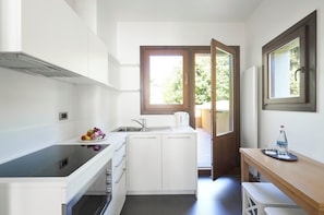 A compact kitchen with white cabinetry, a built-in stove, a sink, and a window with a view of greenery outside.