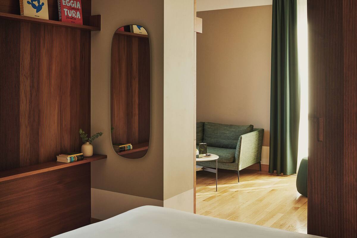 A hotel room with a wooden wardrobe, a mirror, a green sofa, and a small table.
