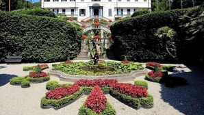 A large, white building with a symmetrical facade, a central entrance with a staircase, and a formal garden with geometric hedges and a statue. - Hotel Belvedere (Bellagio)