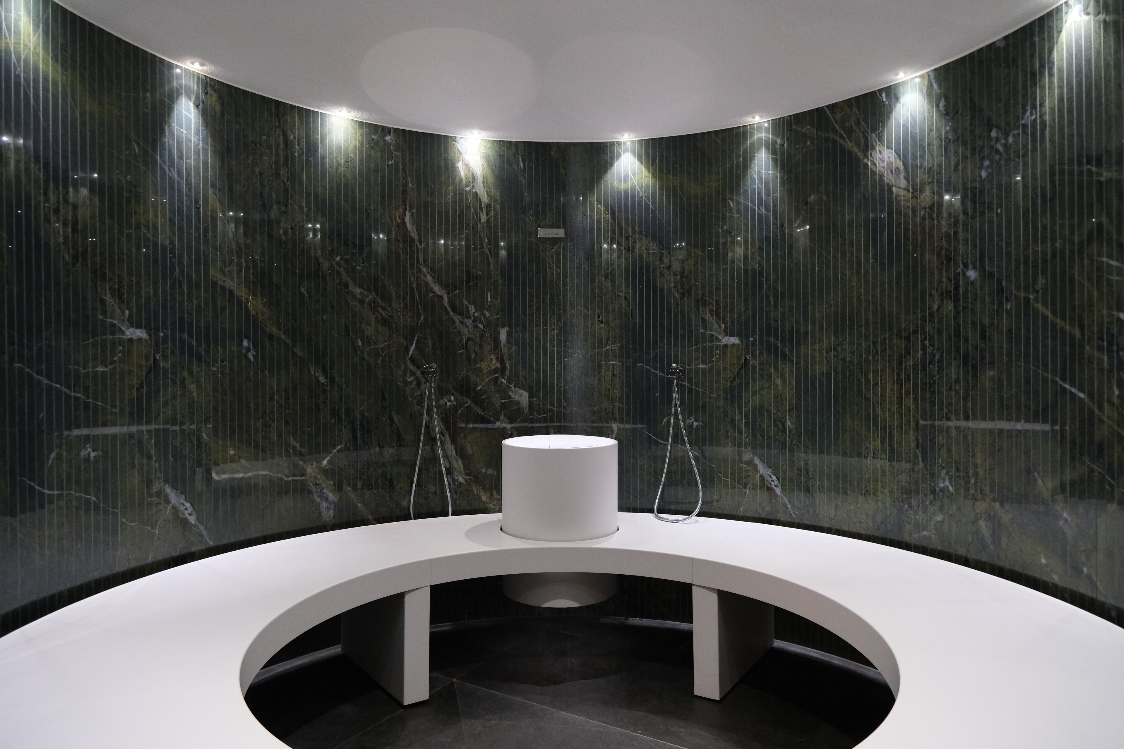 Une salle de bain moderne avec un lavabo blanc aux lignes courbes, des murs en marbre et un plafond au design circulaire.