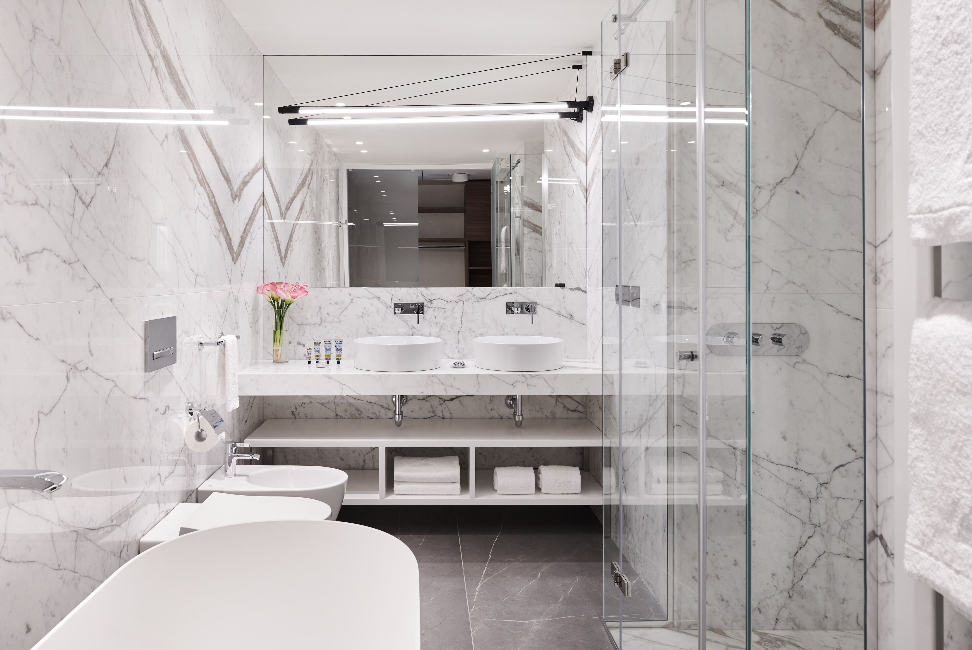 A modern bathroom with marble walls, a glass shower enclosure, and a vanity with two sinks.
