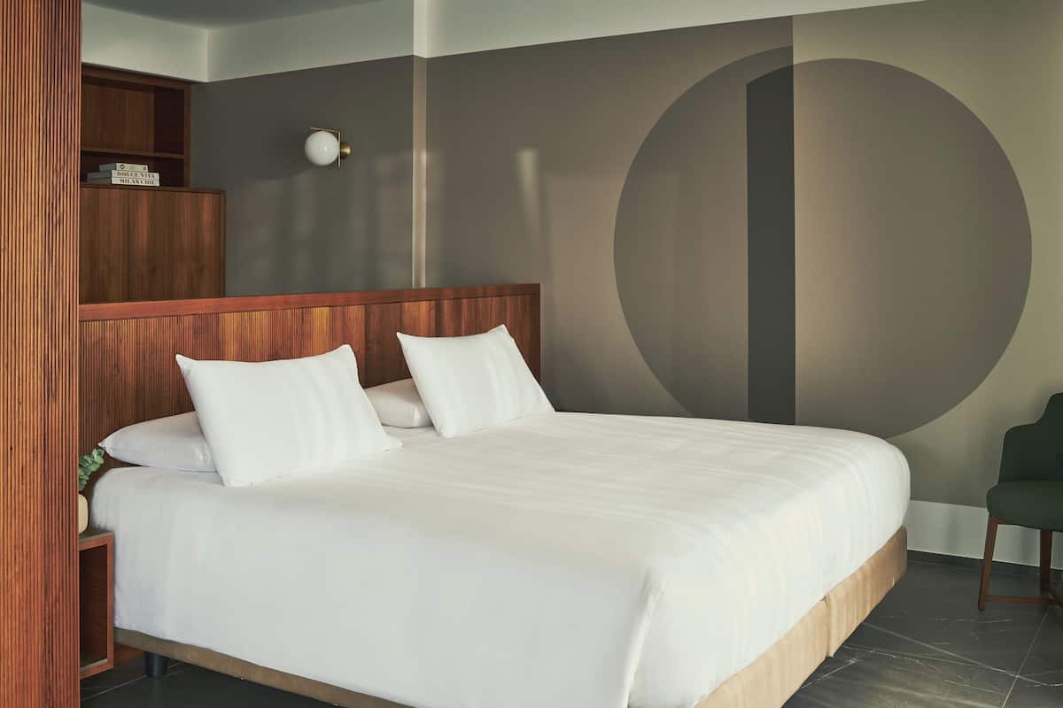 A neatly made bed with white linens and pillows, a wooden headboard, and a large circular wall design.