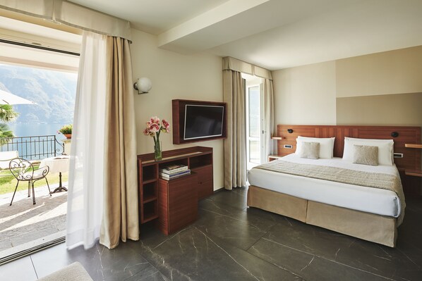 A hotel room with a bed, a TV, a desk with books, and a view of the outdoors.