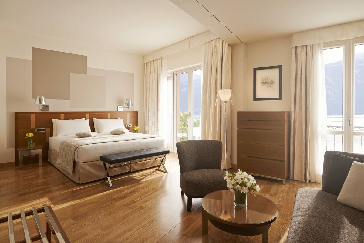 A hotel room with a bed, a chair, a sofa, a table, and a view of the outdoors.