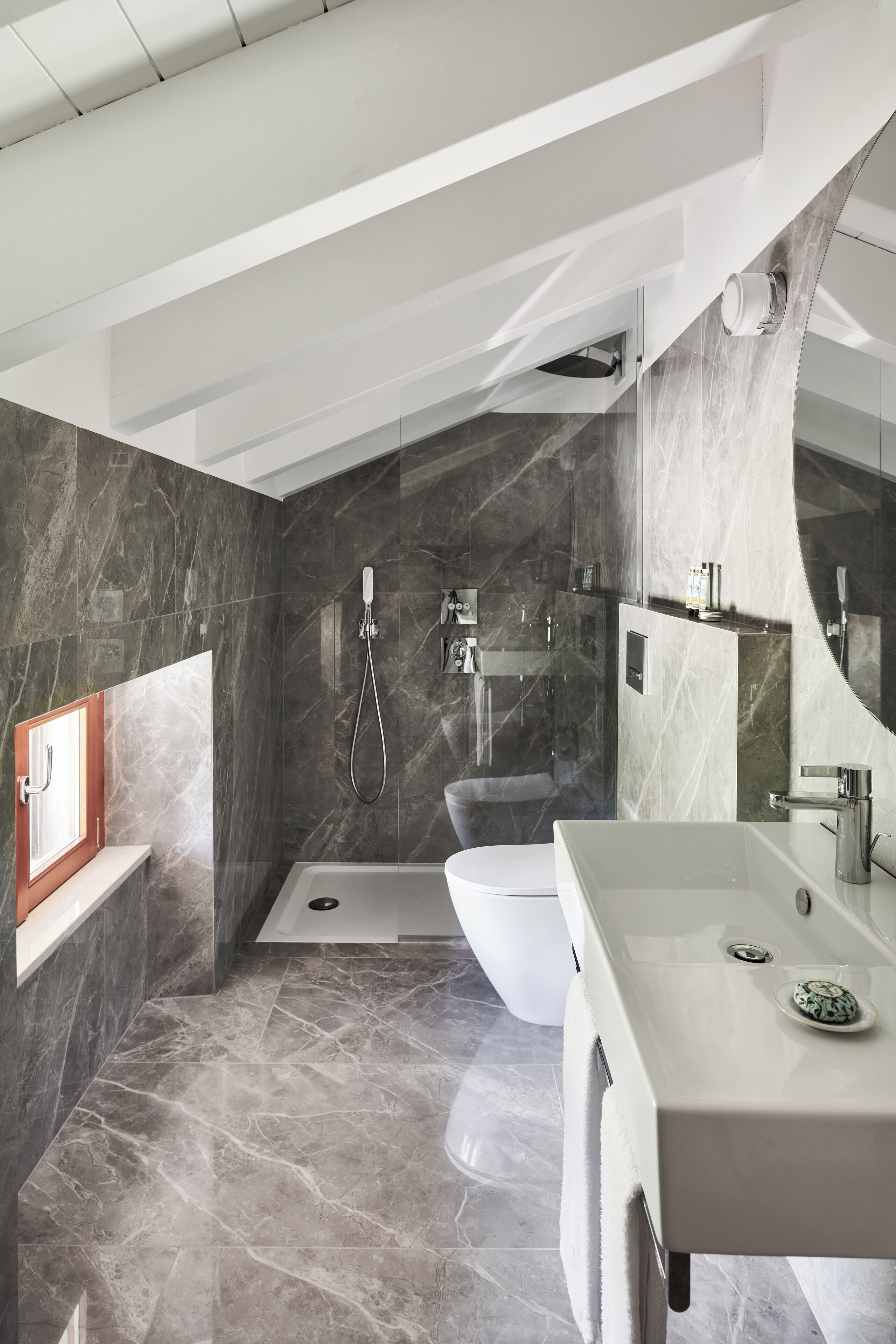 A modern bathroom with a bathtub, toilet, and sink, featuring marble walls and a large mirror.