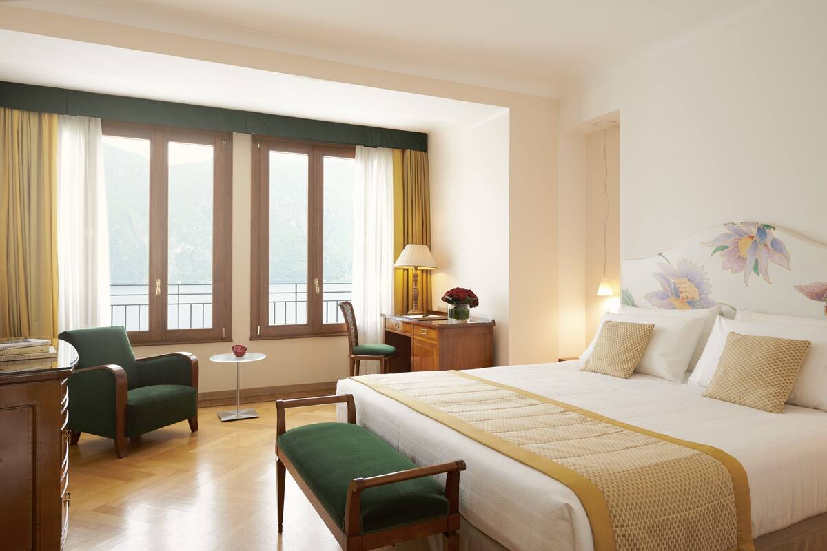 A hotel room with a bed, a desk, a chair, a small table, and a window with curtains.