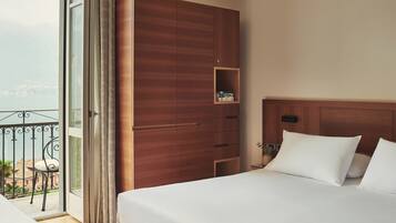A hotel room with a bed, a wooden wardrobe, a small shelf, and a balcony with a view of the city.