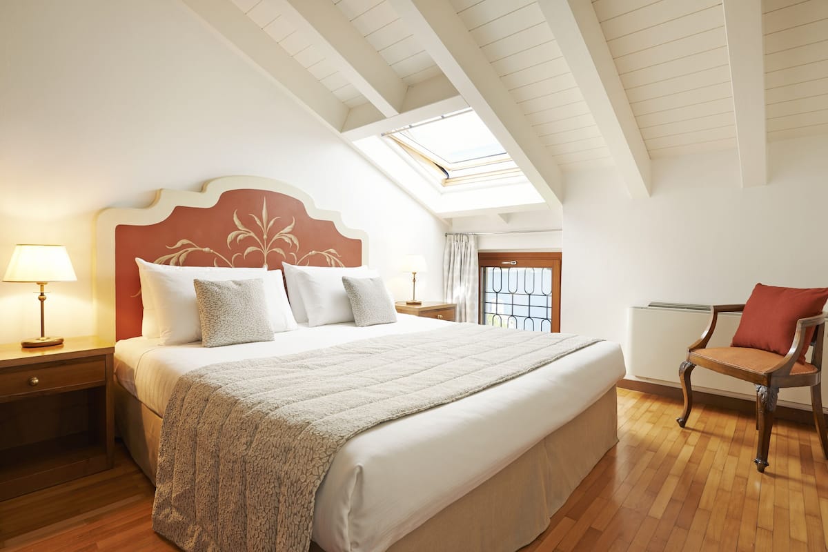 A bedroom with a large bed, a nightstand, a chair, a skylight, and a window.