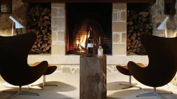 Two modern chairs facing a fireplace with logs, a wooden table, and stone walls.