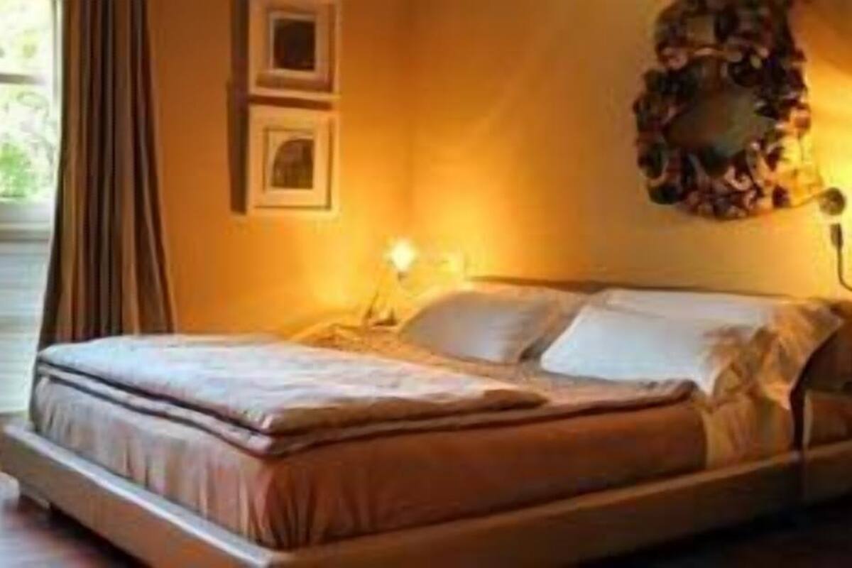 Une chambre à coucher avec un lit, une chaise, une petite table et une fenêtre avec des rideaux.