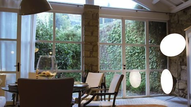 Una habitación con amplias ventanas, paredes de piedra y una mesa redonda con sillas.