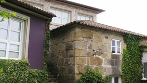 Un edificio de piedra con techo de tejas, muros cubiertos de hiedra y una ventana con marco blanco.