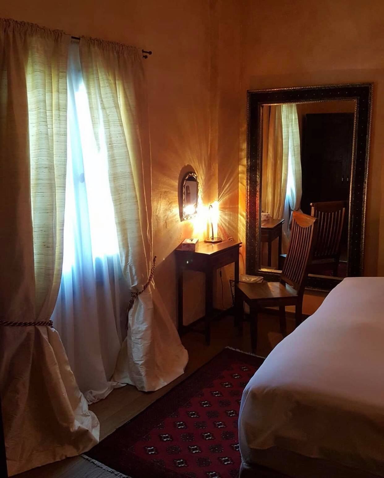 A hotel room with a bed, a desk with a lamp, a chair, and a large mirror.