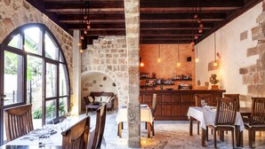 Un intérieur rustique avec des murs en pierre, des poutres en bois, un coin bar avec des bouteilles et un espace repas avec des tables et des chaises.