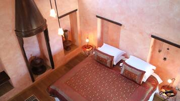 A bedroom with a large bed, a hanging light fixture, a small table with a lamp, and a wall-mounted telephone.