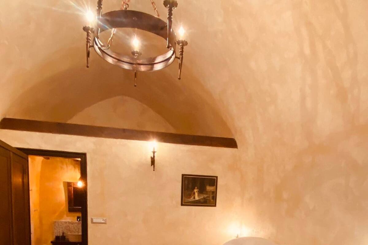 Ein Schlafzimmer mit einem großen Bett, einer Chandelüster, einem gerahmten Bild an der Wand und einer Tür zu einem anderen Raum.
