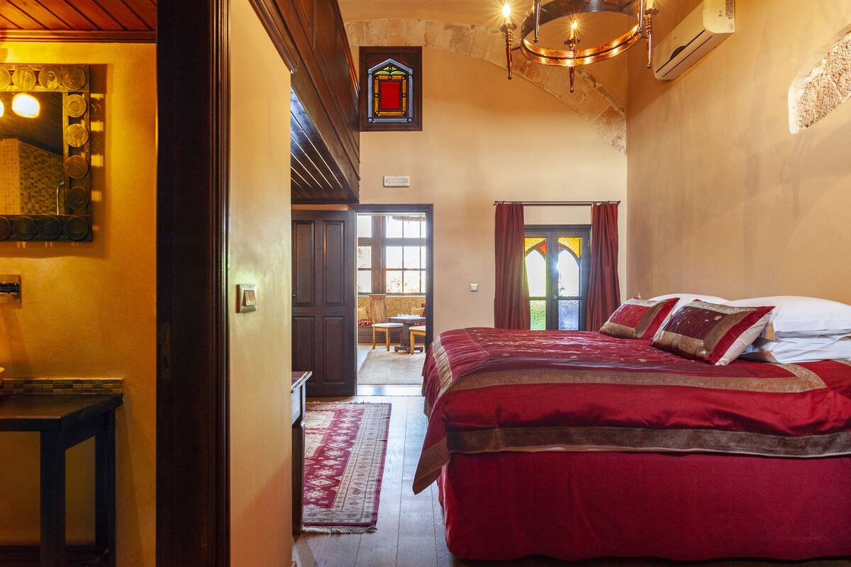 Ein Schlafzimmer mit einem großen Bett, einem Holzkopfbrett, einem Spiegel und einer Chandelüster.