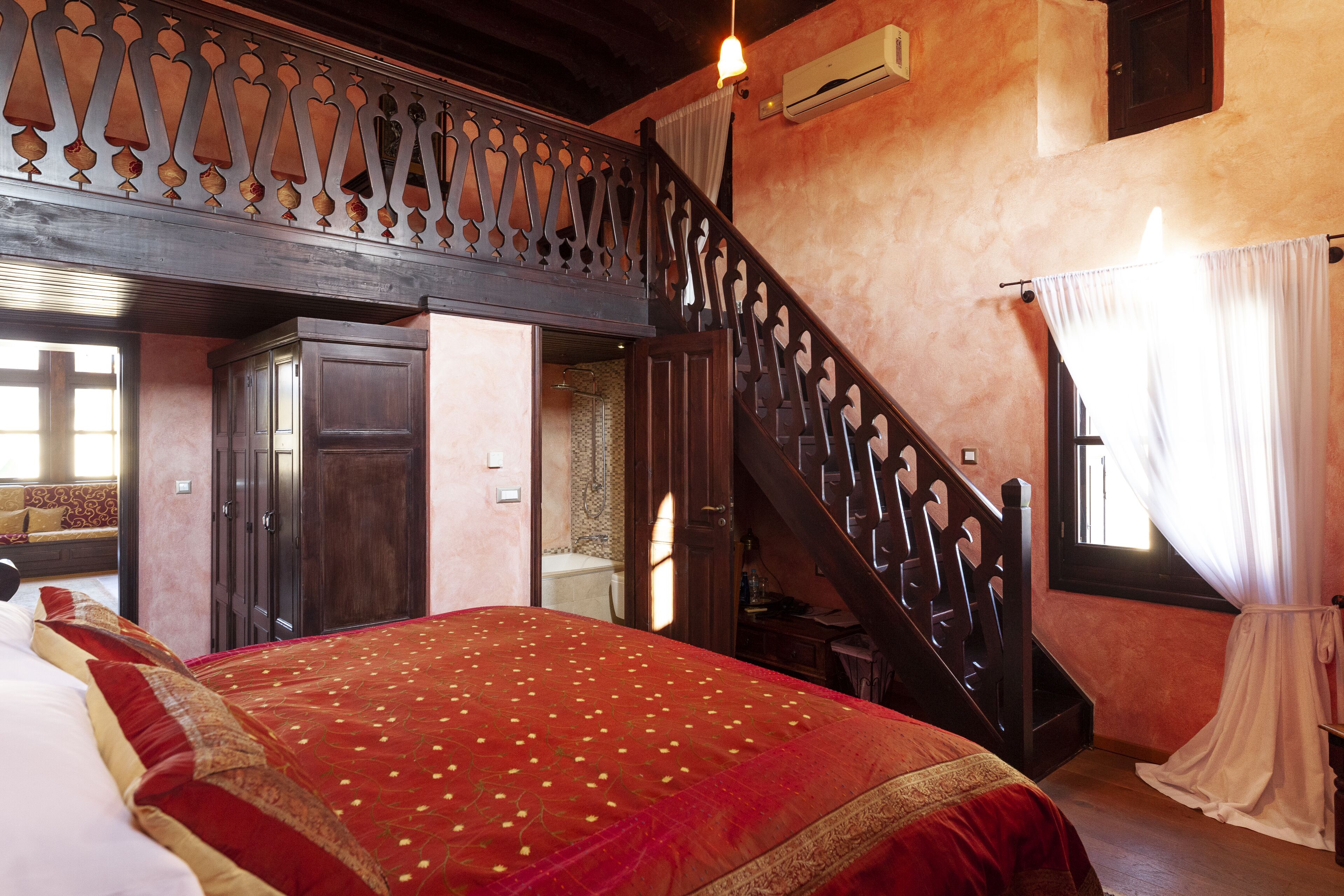 Een slaapkamer met een groot bed, een houten trap en uitzicht op de badkamer.