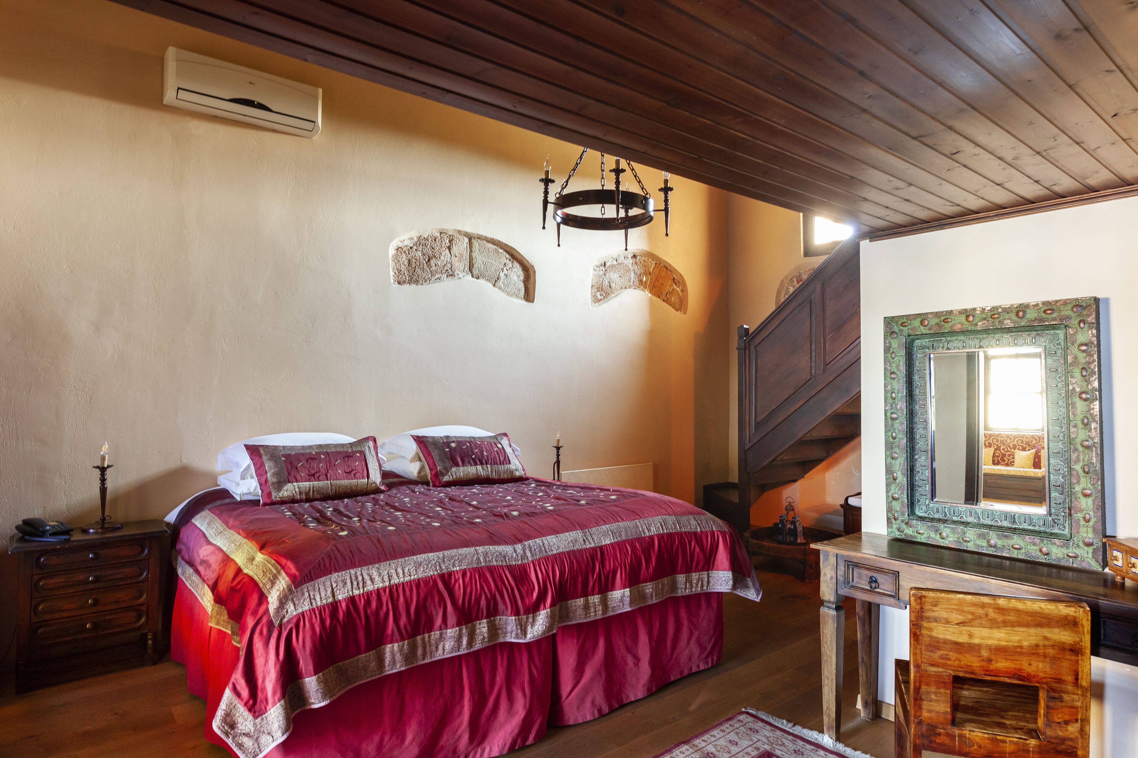 Une chambre à coucher avec un grand lit, une commode en bois, un miroir et un escalier.