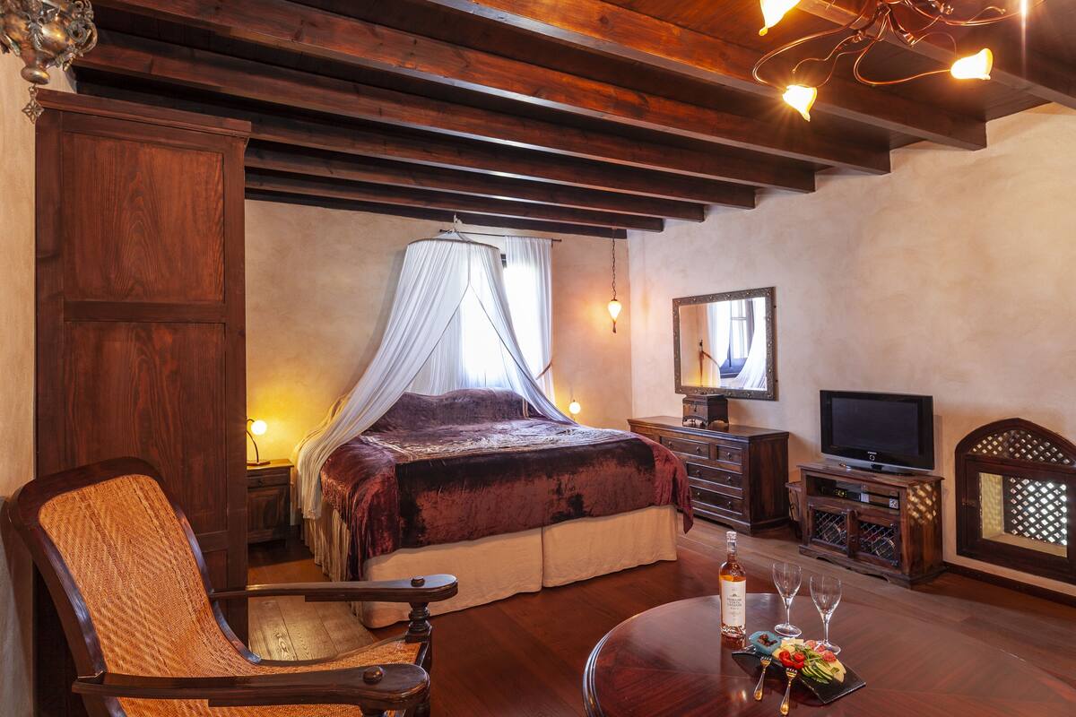 Ein Schlafzimmer mit einem Bett, einem Fernseher, einem Sessel, einem Tisch mit Flasche und Gläsern sowie einem Spiegel.