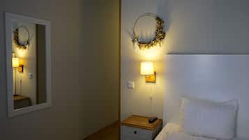 Ett hotellrum med en säng, ett sängbord med en lampa, en spegel som hänger på väggen och en dekorativ krans.