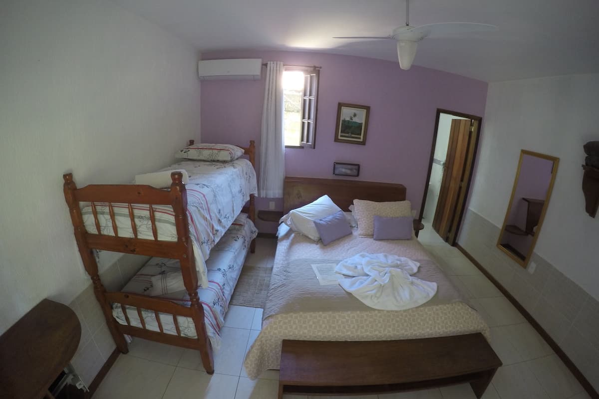 A bedroom with a bunk bed, a single bed, a ceiling fan, a window with curtains, a mirror, and a framed picture on the wall.