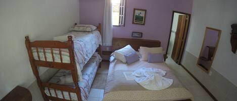 A bedroom with a bunk bed, a single bed, a ceiling fan, a window with curtains, a mirror, and a framed picture on the wall.