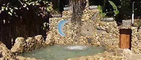 A stone pond with a waterfall, surrounded by rocks and vegetation.
