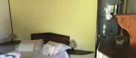 A hotel room with a bed, bedside table, lamp, and a small wooden cabinet.
