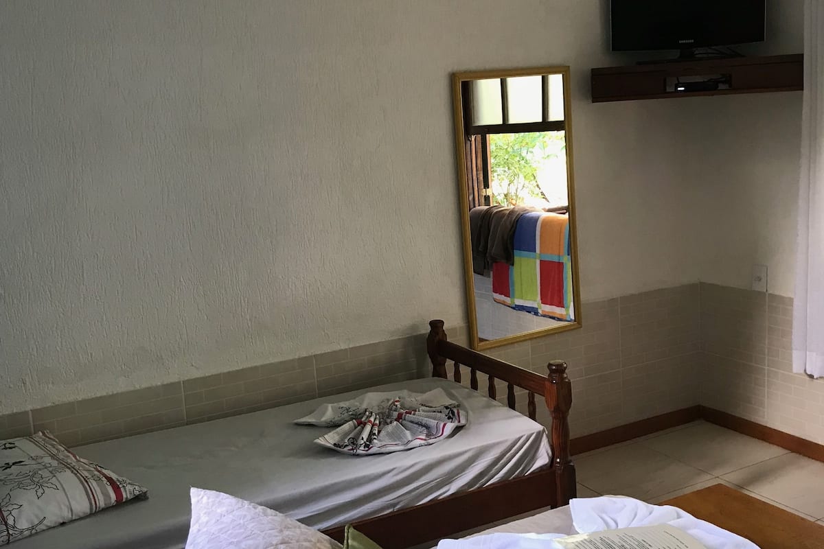 A hotel room with two single beds, a television mounted on the wall, and a window with curtains.