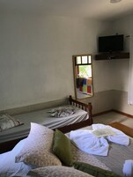 Una habitación de hotel con dos camas individuales, un televisor montado en la pared y una ventana con cortinas.