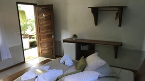 Un lit bien fait, avec des oreillers et des serviettes, un petit réfrigérateur et une étagère en bois au-dessus.