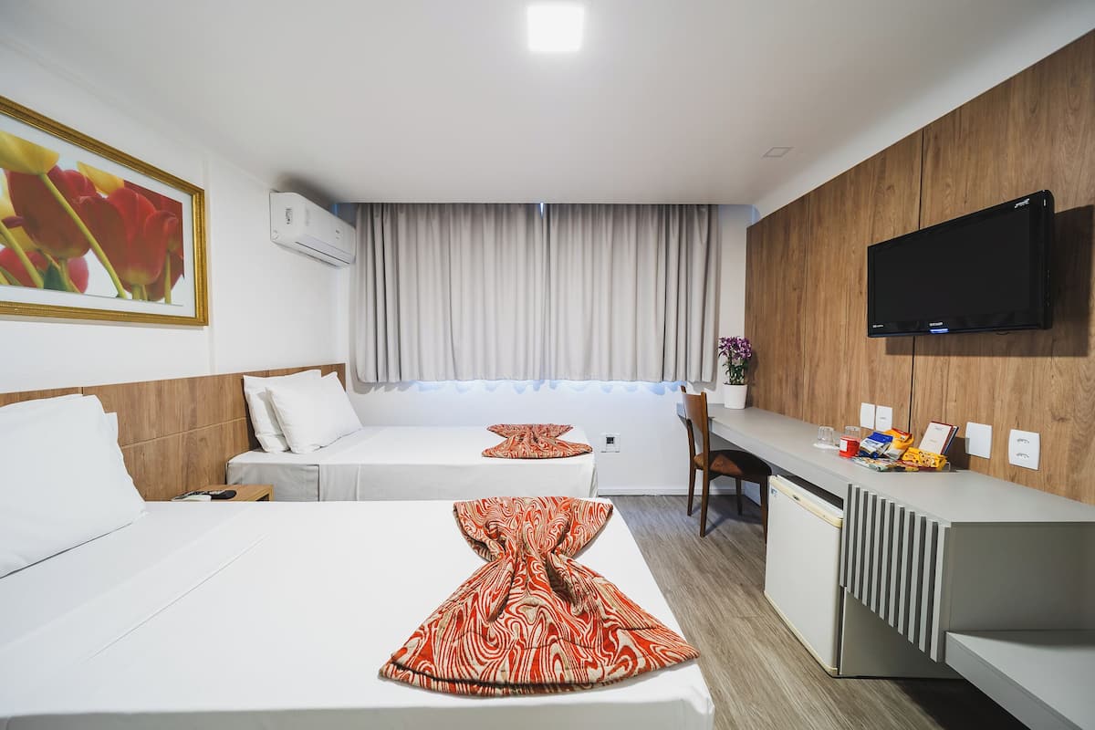 Habitación de hotel con dos camas, un escritorio, un televisor de pantalla plana y un ventanal con cortinas.