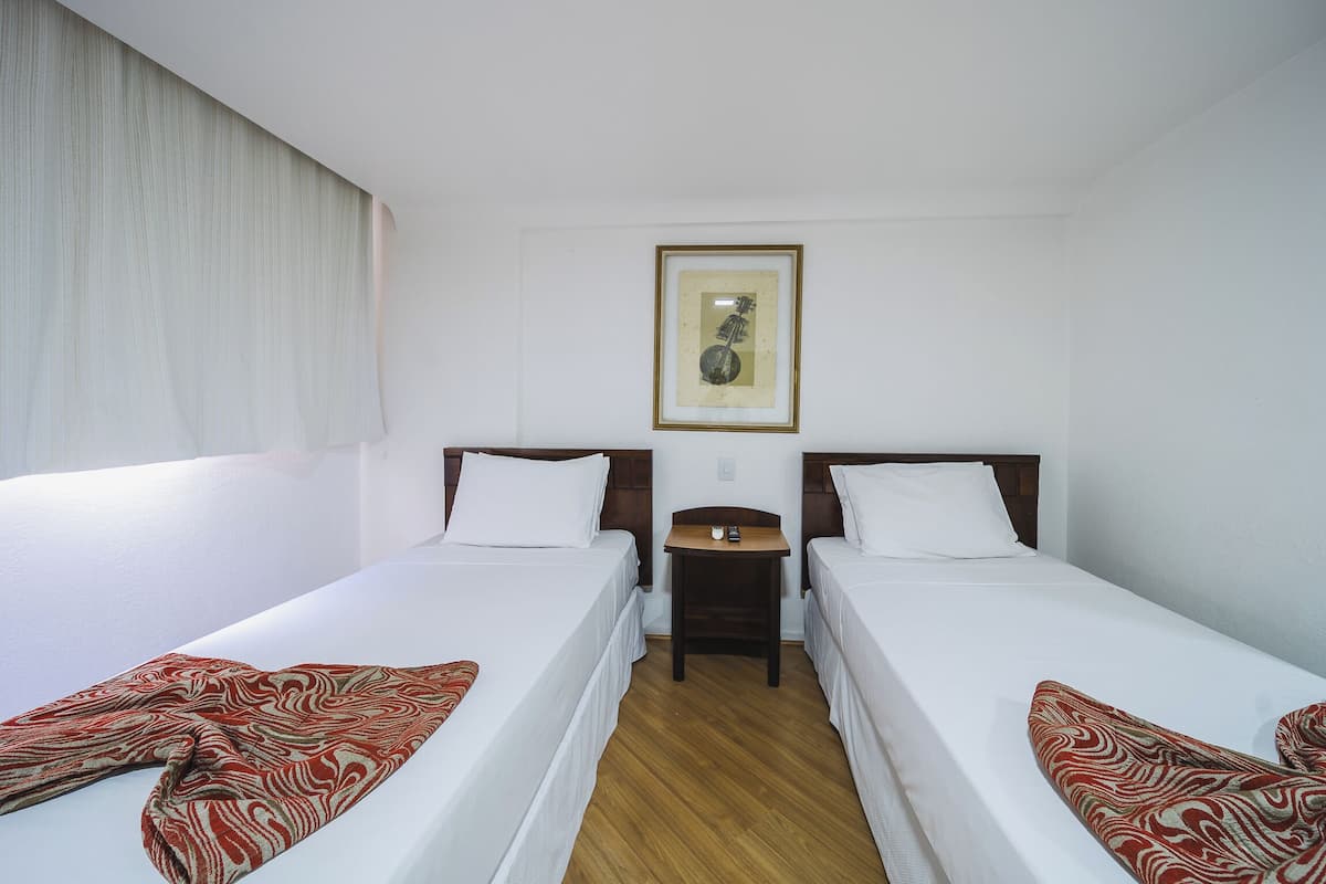Una habitación de hotel con dos camas individuales, una mesita pequeña y un cuadro en la pared.
