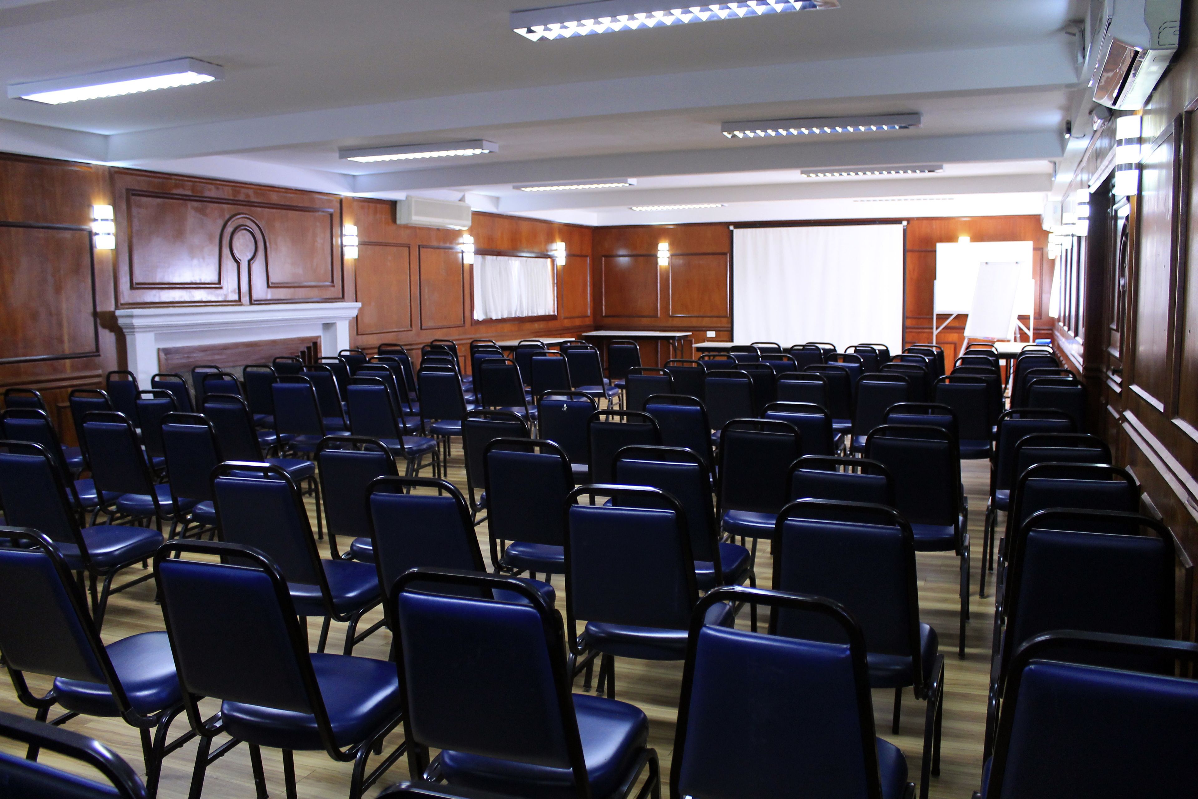 A conference room with rows of black chairs, a wooden panel wall, and a whiteboard.