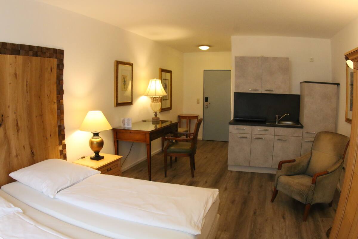 Une chambre d’hôtel avec deux lits, un bureau avec une lampe, une chaise, un coin cuisine et un téléviseur.