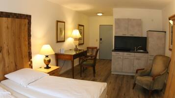 Hotelkamer met twee bedden, een bureau met lamp, een stoel, een kitchenette en een televisie.