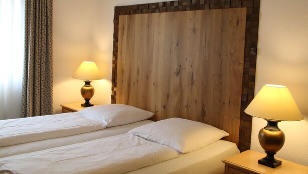 Quarto de hotel com duas camas, painel de cabeceira de madeira e abajures.
