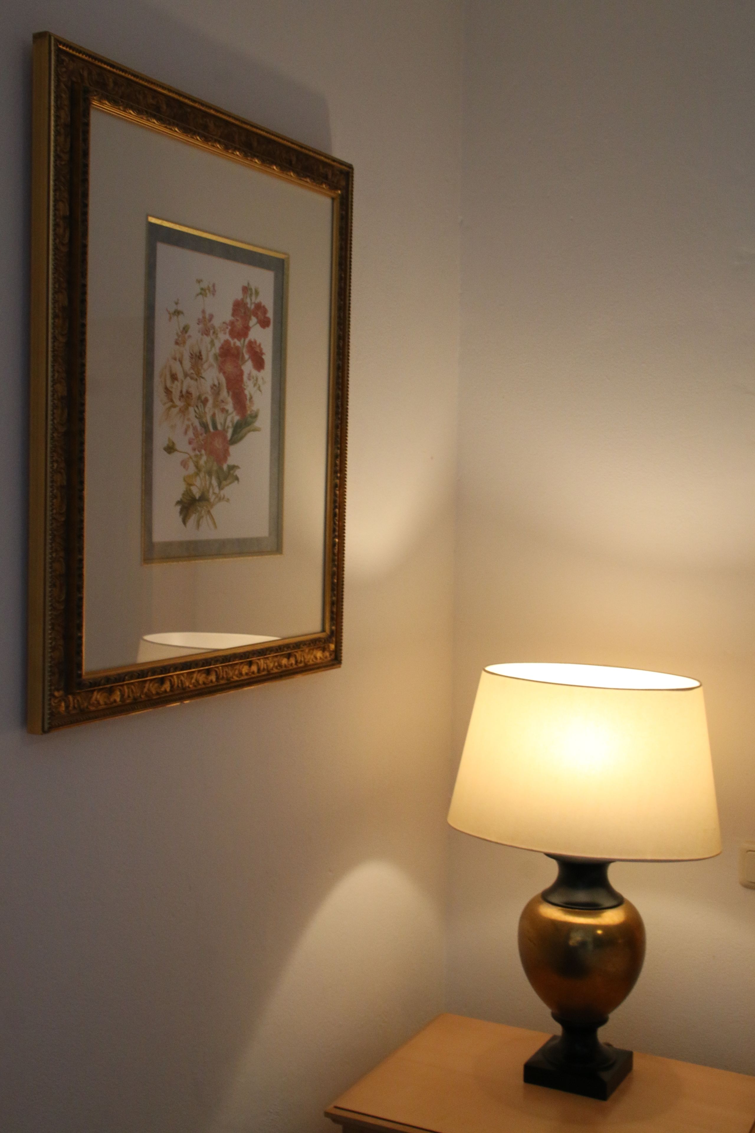 A framed floral artwork on a wall, a table lamp with a white shade, and a small table.