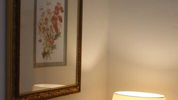 A framed floral artwork on a wall, a table lamp with a white shade, and a small table.