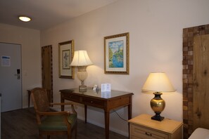 Habitación de hotel con un escritorio de madera, dos lámparas, una silla, un mueble pequeño y dos cuadros en la pared.