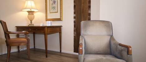 A room with a wooden desk, a chair, a lamp, and a framed picture on the wall.