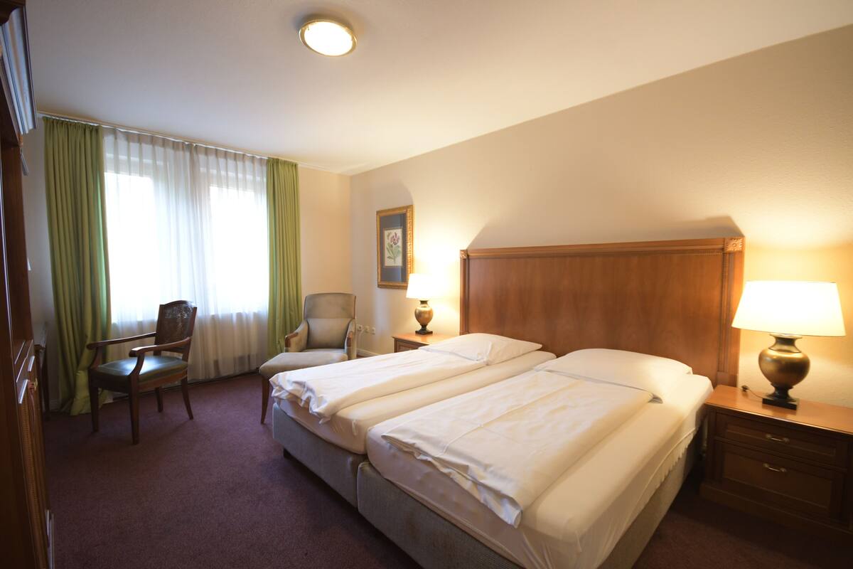 Une chambre d’hôtel avec deux lits, une chaise, un bureau, une lampe et un tableau au mur.