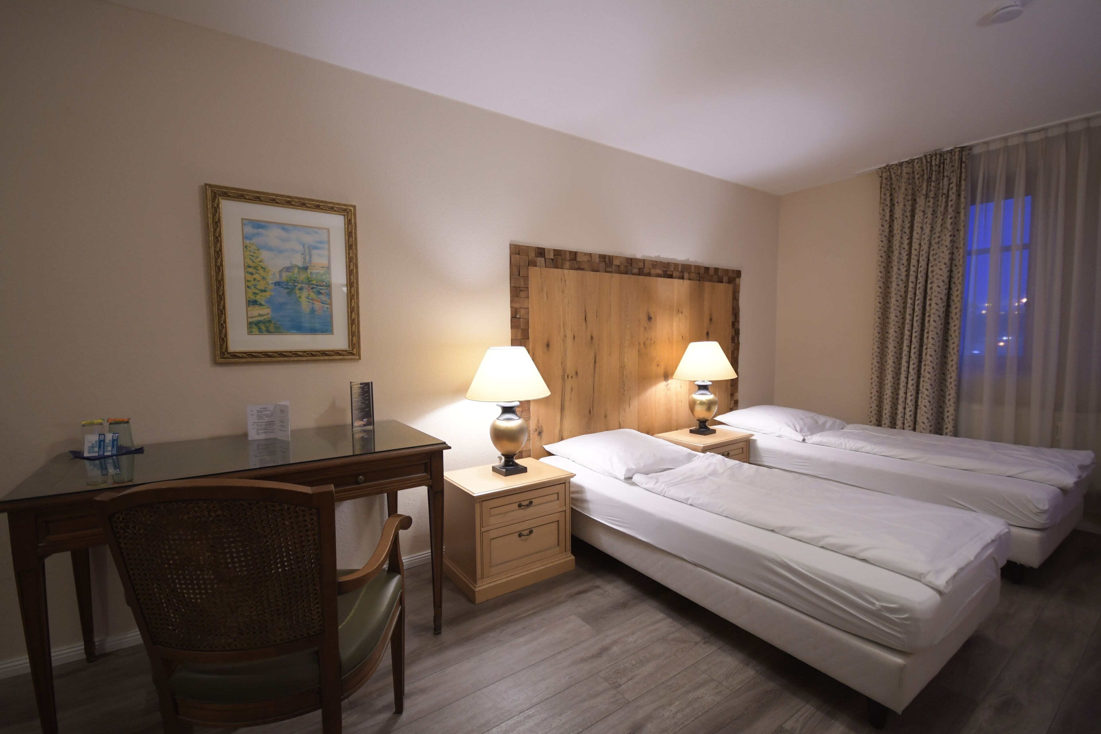 Habitación de hotel con dos camas, un escritorio, una silla y un cabecero de madera.