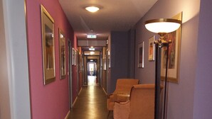 Um corredor de hotel com piso de madeira, quadros nas paredes e uma cadeira com abajur.