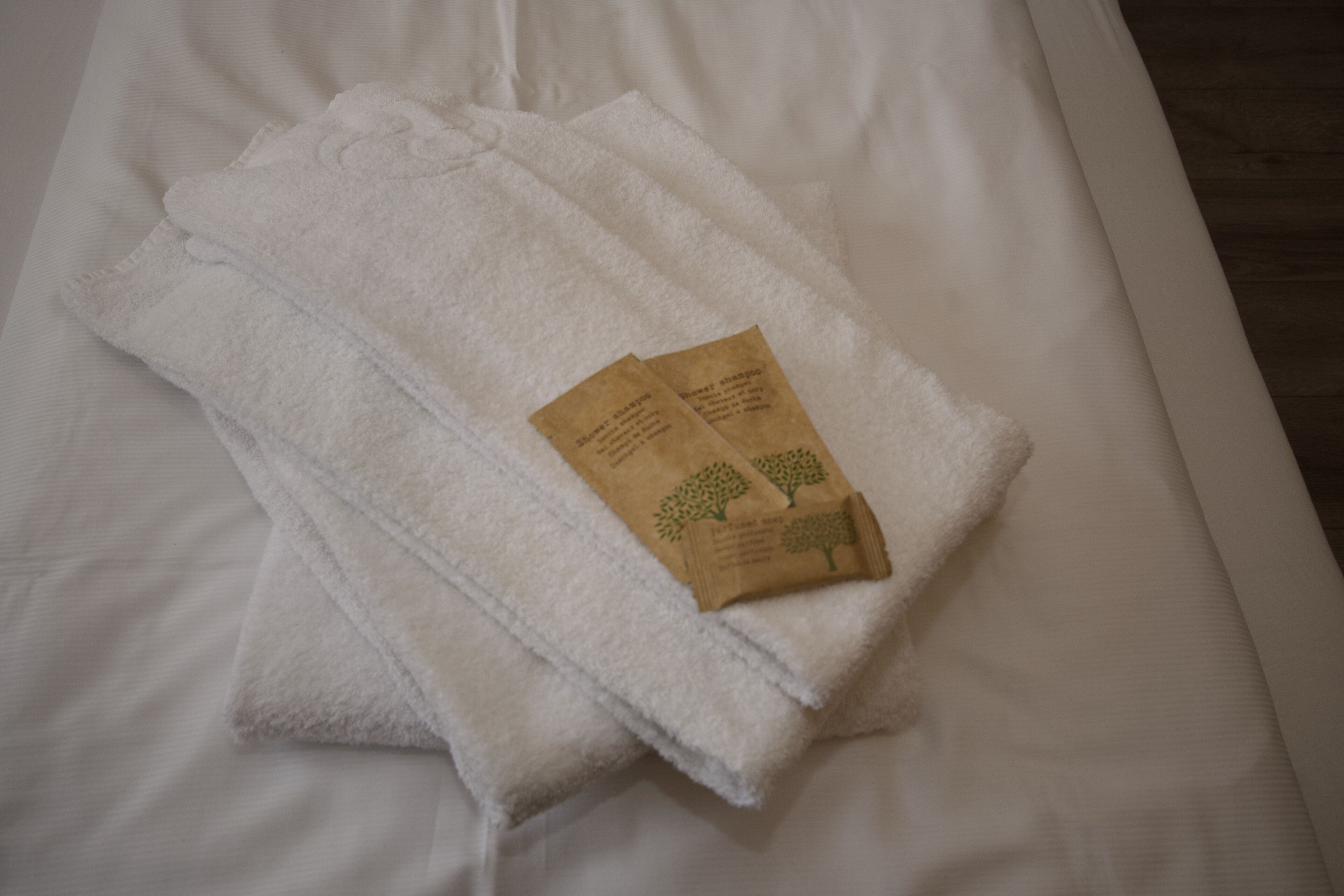 A neatly folded white towel with two small brown cards on a bed.