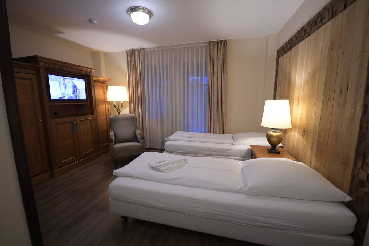 Une chambre d’hôtel avec deux lits, un téléviseur, une chaise et une tête de lit en bois.