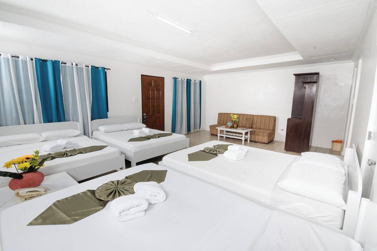 A hotel room with two beds, a sofa, a small table with a vase, and a wooden cabinet.
