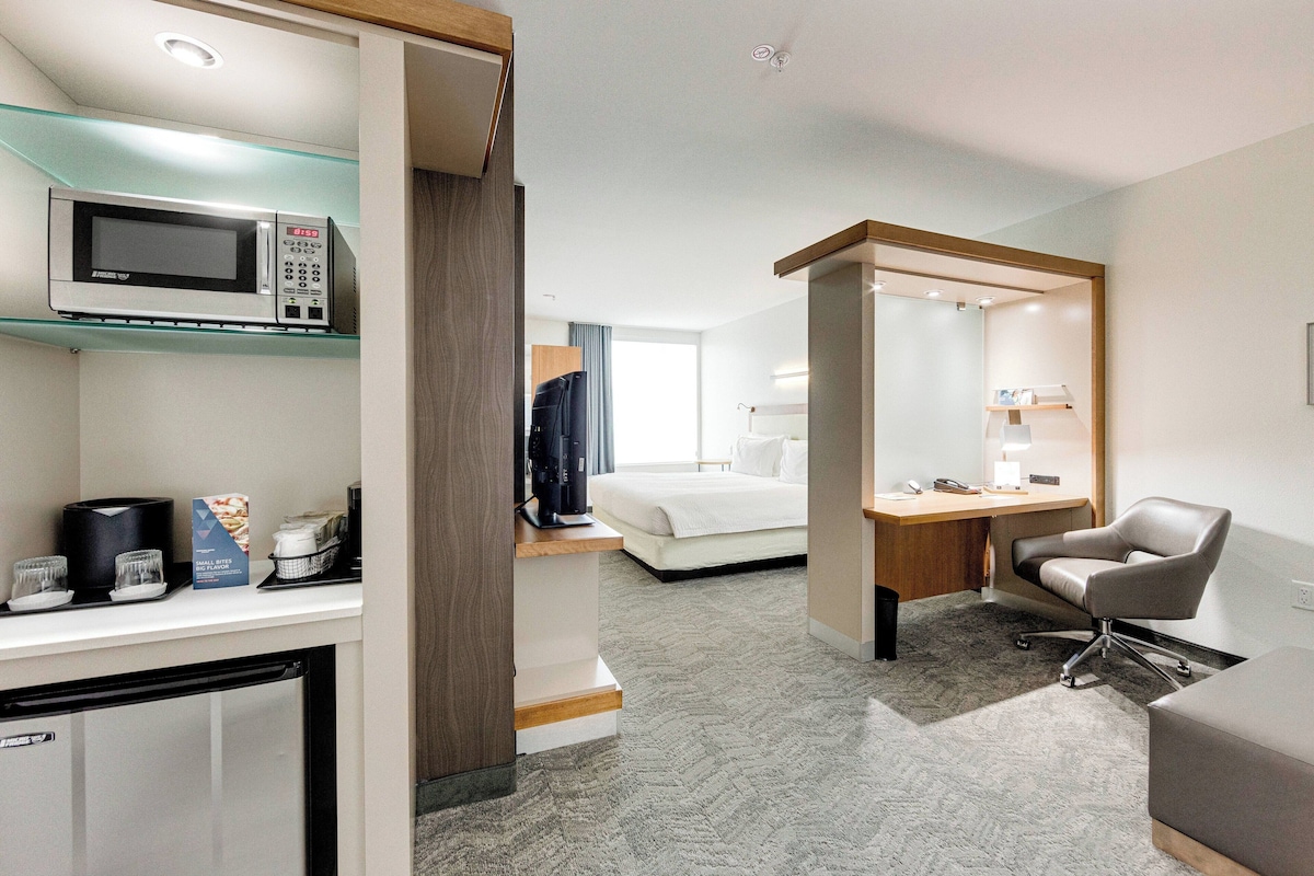 A hotel room with a kitchenette, a bed, a desk, and a chair.